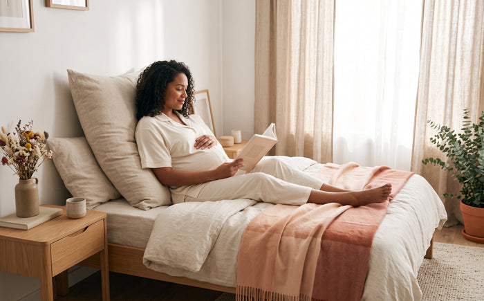Femme enceinte qui lit dans son lit, calée contre un oreiller de grossesse